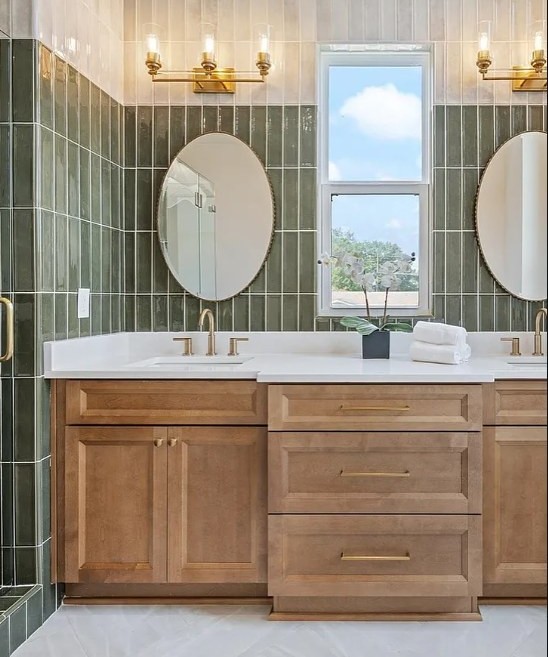 Primary bath with vertical sage tile, double round mirrors and brass sconces